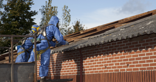 Twee werkmannen verwijderen een golfplaten dak met asbest in
